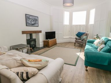 A living room with a beige armchair a green sofa a gray armchair with a throw pillows a framed picture a wood stove and a television at 11 Marine Terrace in Criccieth