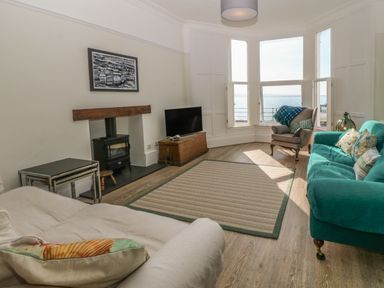 A living room with a fireplace television sofas and a bay window overlooking the sea at 11 Marine Terrace in Criccieth
