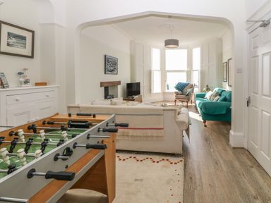 A living room with a foosball table, sofas, armchair, television, and large bay windows at 11 Marine Terrace in Criccieth