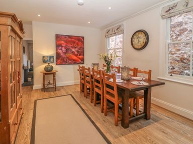 A dining room with a wooden table and chairs a clock on the wall and a cabinet at 11 Marine Terrace in Criccieth