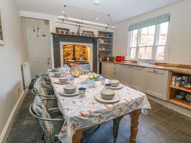 A kitchen with a dining table set for eight near a stove and cabinets under a window at 11 Marine Terrace in Criccieth