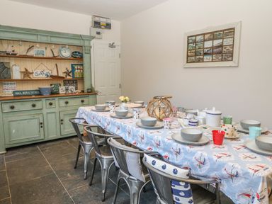 A dining room with a table set for a meal and a cupboard with nautical decorations at 11 Marine Terrace in Criccieth