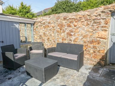 An outdoor patio area with stone wall black wicker seating and a black wicker coffee table at 11 Marine Terrace in Criccieth