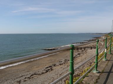 A coastal walkway with green railings overlooking a pebble beach and the sea at 11 Marine Terrace in Criccieth