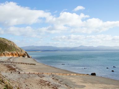 A pebble beach with wooden groynes and a steep cliff on the left with mountains in the distance at 11 Marine Terrace in Criccieth