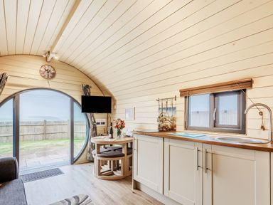 A kitchen and dining area with round window and sliding door leading outside at Corndon Pod in White Grit near Chirbury