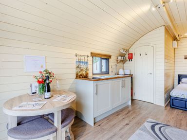 A kitchen area with a small dining table and chairs inside a wooden pod at Corndon Pod White Grit near Chirbury