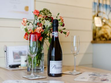 A bottle of prosecco with two empty champagne glasses and a vase of flowers on a wooden table at Corndon Pod in White Grit near Chirbury