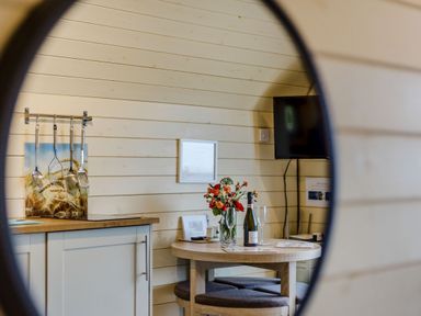 A kitchen area with hanging utensils and a table with a bottle, glasses, and flowers at Corndon Pod in White Grit near Chirbury