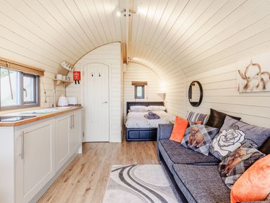 A narrow living space with a kitchen on the left a sofa with cushions and a bed at Corndon Pod White Grit near Chirbury
