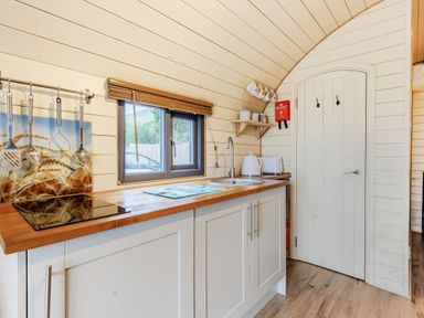 A kitchen with wooden countertops a sink a window hanging kitchen utensils and a closed door at Corndon Pod in White Grit near Chirbury