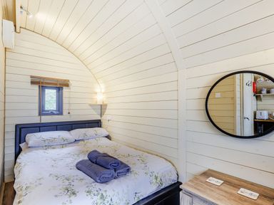 A bedroom with a double bed with folded towels on it a round mirror and a wooden dresser at Corndon Pod White Grit near Chirbury