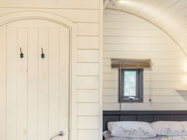 A wooden arched door with two hooks and a bed with pillows near a small window at Corndon Pod in White Grit near Chirbury