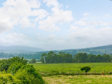 A countryside landscape with green fields trees and distant hills under a cloudy sky at Corndon Pod White Grit near Chirbury