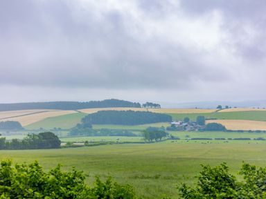 A view of fields trees and farmland with farm buildings under a cloudy sky at Corndon Pod in White Grit near Chirbury