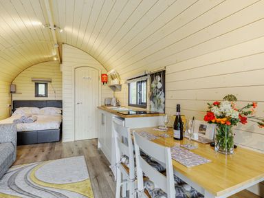 An open plan pod interior with a bed sofa kitchenette and dining table with flowers at Stiperstones Pod White Grit near Chirbury