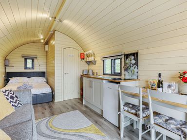 An interior view of a wooden pod with a bed at the back a kitchenette with a fridge and sink and a dining table with two chairs at Stiperstones Pod in White Grit near Chirbury