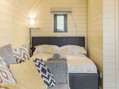 A bedroom with a bed, patterned cushions on a sofa, and a small window at Stiperstones Pod in White Grit near Chirbury