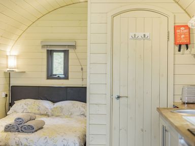 A bedroom with a double bed with towels on it a window a wooden door and part of a kitchen counter at Stiperstones Pod in White Grit near Chirbury