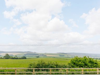 A rural landscape with green fields hedges and a wooden fence under a cloudy sky at Stiperstones Pod in White Grit near Chirbury