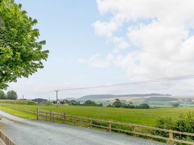A rural landscape with a gravel path and wooden fence alongside green fields and distant hills at Stiperstones Pod in White Grit near Chirbury