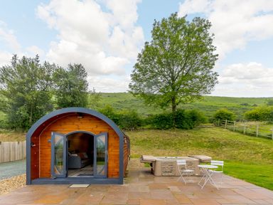 A wooden pod with open double doors next to a hot tub and white outdoor table and chairs at Stiperstones Pod in White Grit near Chirbury
