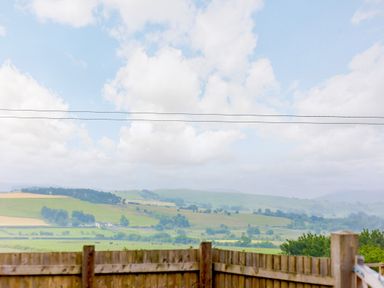 A countryside landscape with green fields and hills behind a wooden fence at Stiperstones Pod in White Grit near Chirbury