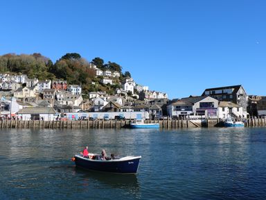 A boat with people on water near a harbor with buildings and houses on a hillside at Downlea in Looe