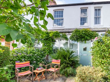 Front garden with two striped chairs and a small table in front of a white house with a green door at Downlea in Looe