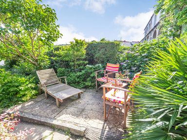 A garden patio with wooden chairs and a table surrounded by green plants at Downlea in Looe