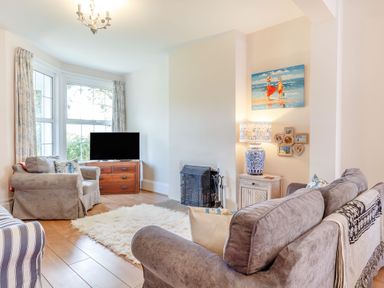A living room with sofas a TV on a wooden chest a lamp and a painting at Downlea in Looe