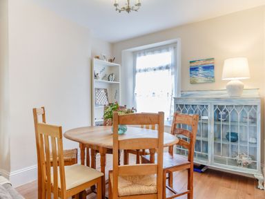 A dining room with a wooden table and chairs a painted cabinet and a window at Downlea in Looe