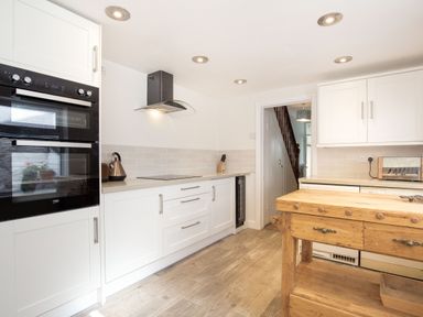 A kitchen with white cabinets a wooden island an oven a kettle and a toaster at Downlea in Looe