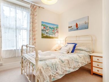 A bedroom with a metal bed frame bedside tables and paintings on the wall at Downlea in Looe
