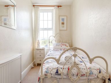 A small bedroom with a single metal bed a bedside table and a window with curtains at Downlea in Looe