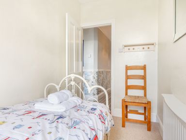 A small bedroom with a single bed with patterned bedding two folded towels a wooden chair and an open door at Downlea in Looe