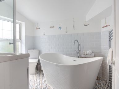 A bathroom with a freestanding bathtub a toilet a sink and patterned floor tiles at Downlea in Looe
