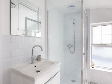 A bathroom with a sink and mirror next to a glass shower enclosure and window at Downlea in Looe