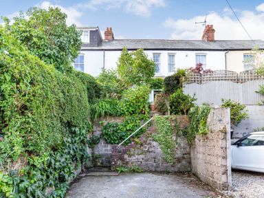 A white terraced house with a garden surrounded by greenery and a small staircase leading to the entrance at Downlea in Looe