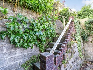 An outdoor stone staircase with brick sides covered in plants and greenery at Downlea in Looe