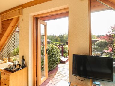 A room with a wooden door open to a garden patio and a television mounted on the wall at Swallow Lodge in Amble