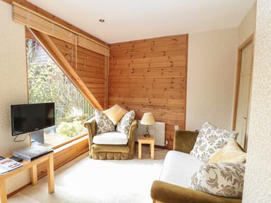 A living room with green armchairs and a sofa near a large window and a small wooden table with a lamp at Swallow Lodge in Amble