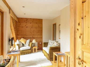 A sitting area with two armchairs a lamp and wooden side tables in a room with wooden paneling at Swallow Lodge in Amble