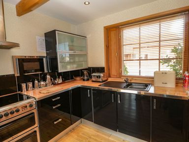 A kitchen with black cabinets wooden countertop stove toaster and a window with blinds at Swallow Lodge in Amble