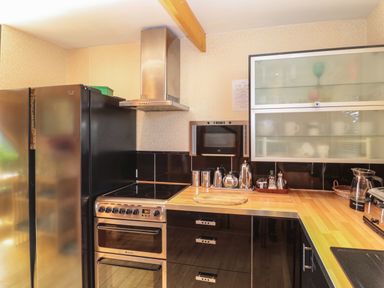 A kitchen with black cabinets wooden countertops a stove refrigerator and glass upper cabinets at Swallow Lodge in Amble
