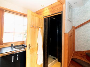 A small kitchen area with a sink next to a wooden door leading to a shower near a wooden staircase with floral wallpaper at Swallow Lodge in Amble