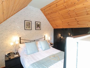 A bedroom with a double bed with two light blue pillows and a heart shape on the bed at Swallow Lodge in Amble