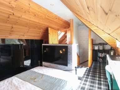 A bedroom with a bed a television mounted on a partition and a desk with a chair at Swallow Lodge in Amble