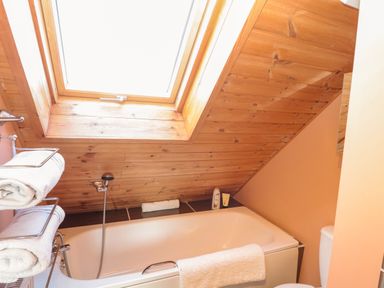 A bathroom with a bathtub under a skylight window and shelves holding towels at Swallow Lodge in Amble