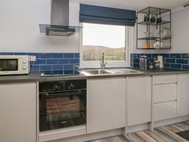 A kitchen with a microwave oven stovetop sink window and blue tiled backsplash at Haka Lodge in Devil's Bridge